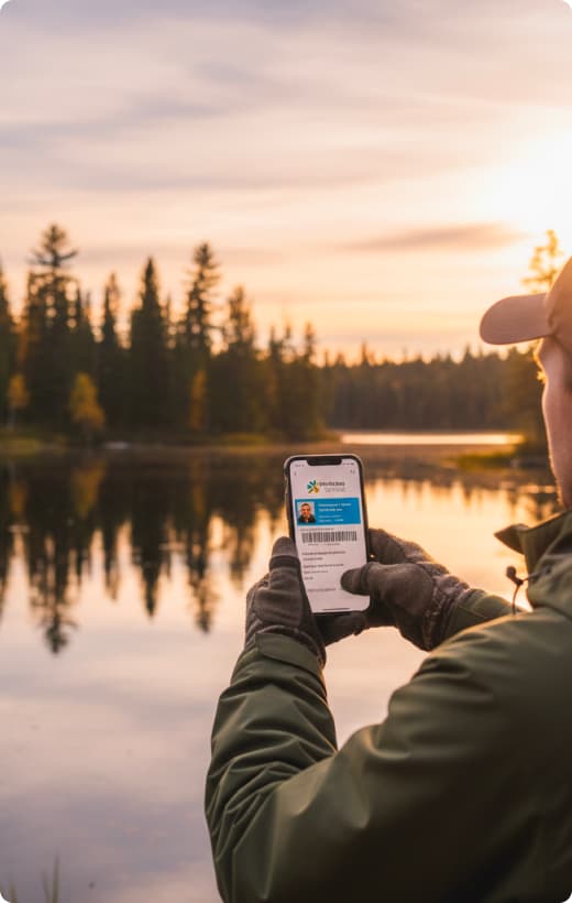 Person holding a fishing licence beside a lake at sunrise